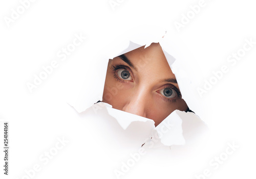 Surprised woman face. Cute attractive woman looking through hole. Copy space for advertising, to insert text or slogan. Discount, sale. © shchus