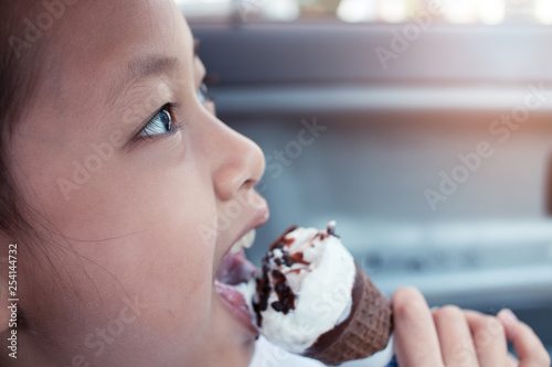 Happy asian little girl eating ice-cream in a milk and chocolate cone in car.