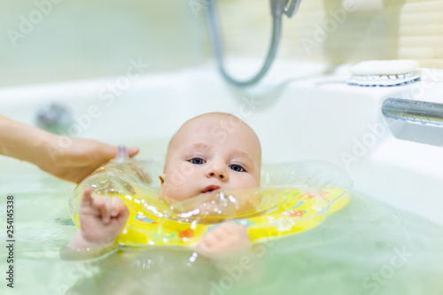 Cute little infant boy swimming with inflatable neck swim ring in bath. Baby having fun during water hygienic activities. Child healthcare and development concept photo