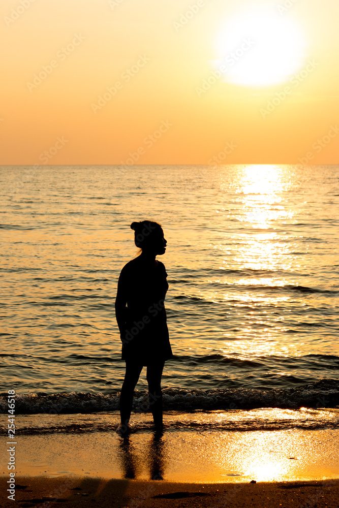 1 woman is standing at the beach when sun set.silhouette