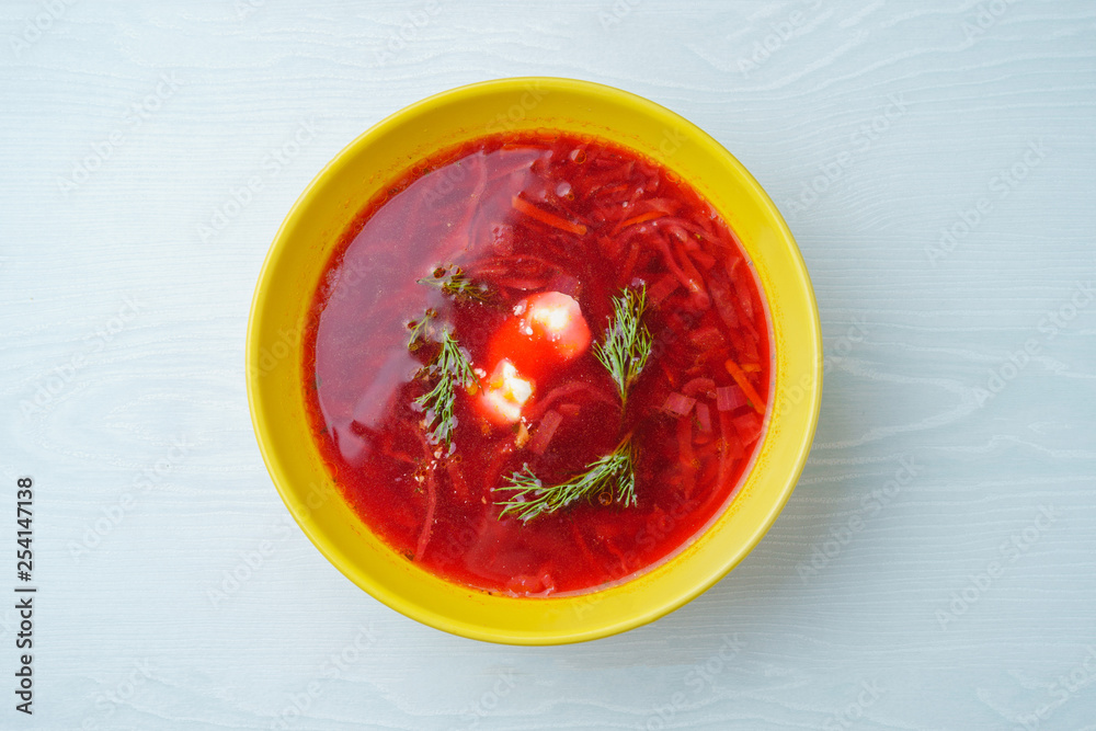 A plate of borsch with sour cream and herbs in a yellow plate on a white table A plate of borsch with sour cream and herbs in a yellow plate on a white table