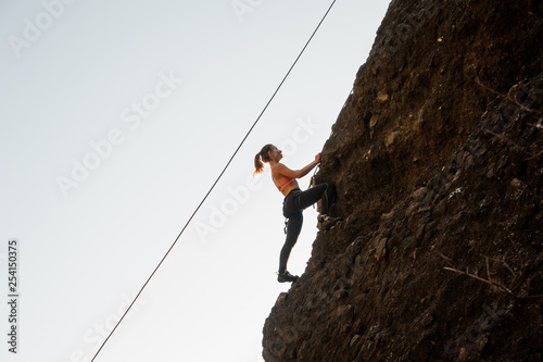 Woman equipped with a rope climbing on the sloping rock