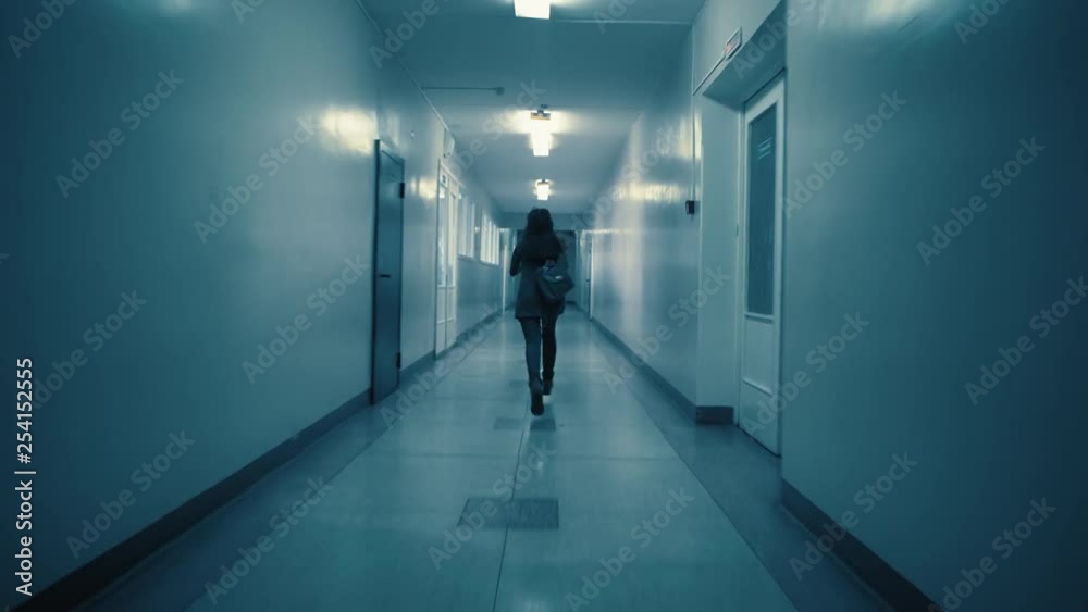 A young excited woman in a panic runs away from her pursuer along a dark corridor. A flickering sign with Russian text above the doors: exit.