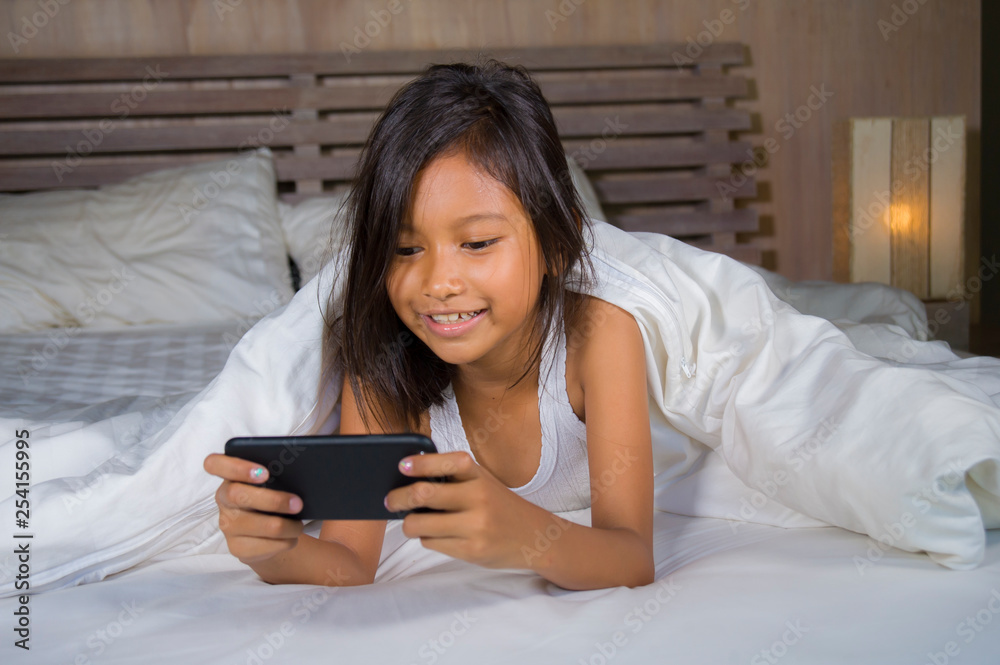 happy and beautiful 7 years old child having fun playing internet game with mobile phone lying on bed cheerful and excited in young girl and technology concept happy and beautiful 7 years old child having fun playing internet game with mobile phone lying on bed cheerful and excited in young girl and technology concept