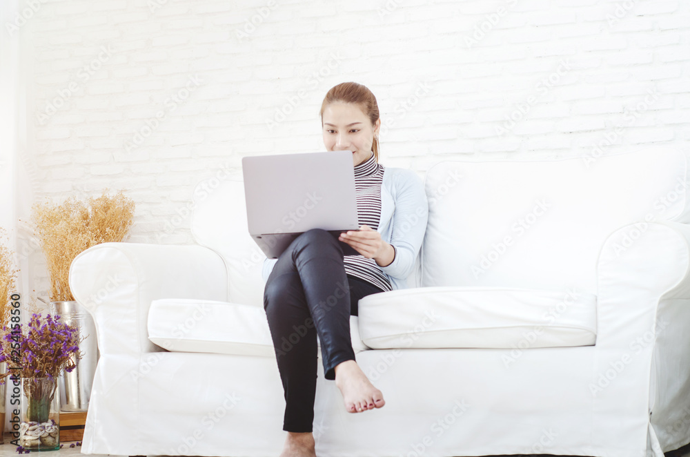 Beautiful Asian woman is smiling.Asian women work with gray laptops on the sofa in the room in the morning. Beautiful Asian woman is smiling.Asian women work with gray laptops on the sofa in the room in the morning.