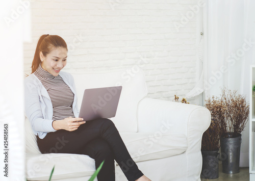Beautiful Asian woman is smiling.Asian women work with gray laptops on the sofa in the room in the morning.She is happy to get a new job, success, or get good news.