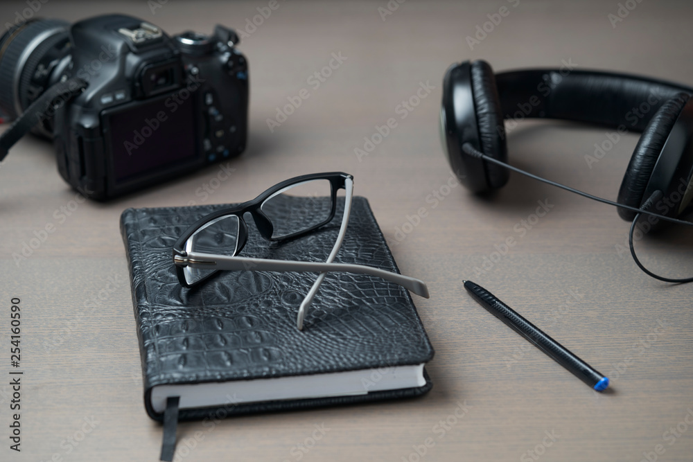 Diary, glasses, headphones, a camera on a wooden table. Workplace of a creative person. Diary, glasses, headphones, a camera on a wooden table. Workplace of a creative person.
