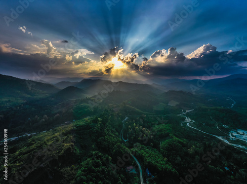 Panoramic aerial landscape of green tropical mountains with flowing river and forest at dramatic cloudy sunset 