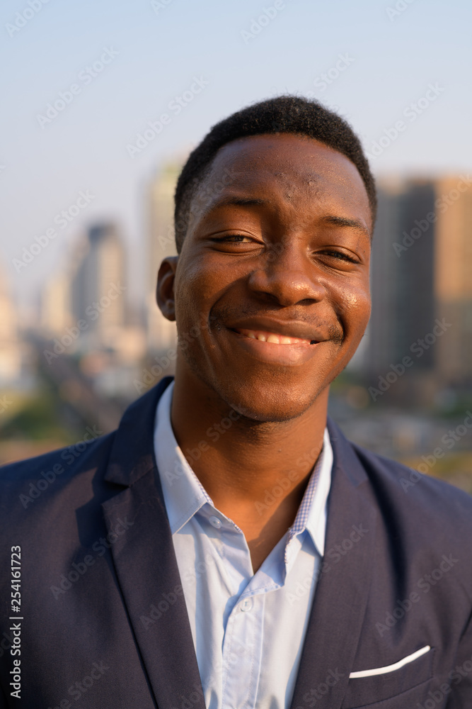Face of young happy African businessman smiling against view of the city Face of young happy African businessman smiling against view of the city