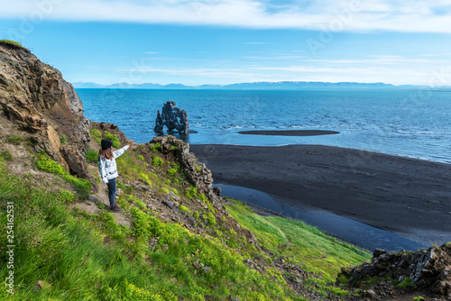 Girl tourist looking at Hvitserkur basalt stack washed with waters of Hindisvik bay in Northwest Iceland. photo