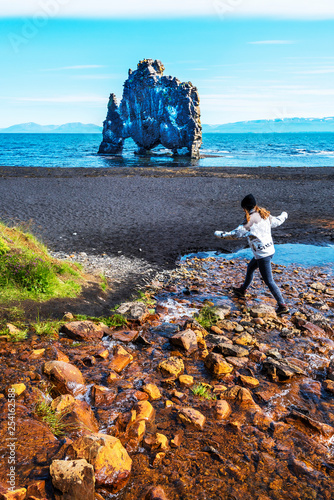 Girl teenager is jumping over water stream in the border of Hindisvik bay in Northwest Iceland, the Hvitserkur basalt stack is at background. photo