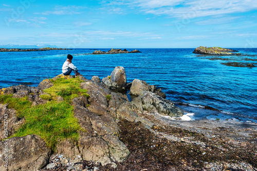 Girl teenager is siting in the border of Hunar Bay looking at wild landscape of western shore of Vatnsnes peninsula in Northwest Iceland. photo