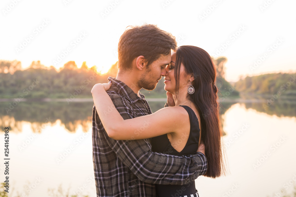 Fototapeta premium Relationship, love and nature concept - Close up portrait of attractive woman and handsome man hugging on the background of the lake