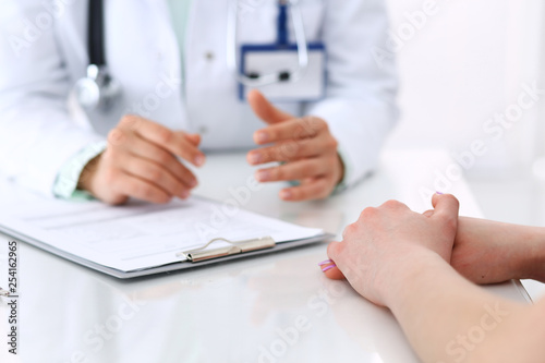 Unknown doctor and patient talking while sitting at the desk in hospital office  close-up of human hands. Medicine and health care concept