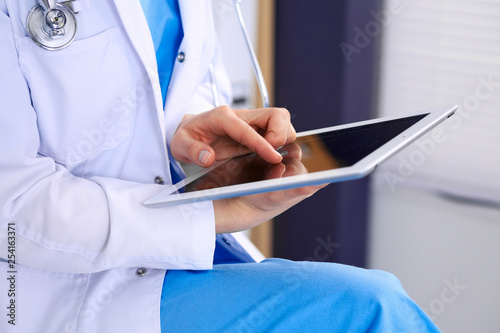 Woman doctor using white tablet computer while sitting at chair in hospital, close-up photo