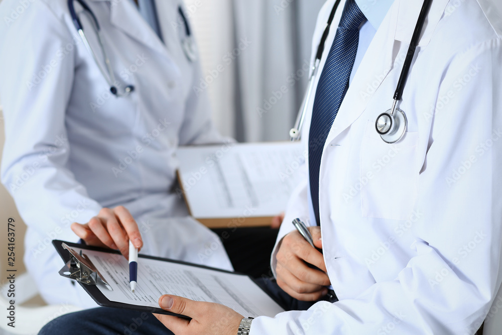 Two unknown doctors filling up medical form on clipboard, just hands closeup. Physicians asking question to patient or discussing medication program. Healthcare, insurance and medicine concept Two unknown doctors filling up medical form on clipboard, just hands closeup. Physicians asking question to patient or discussing medication program. Healthcare, insurance and medicine concept