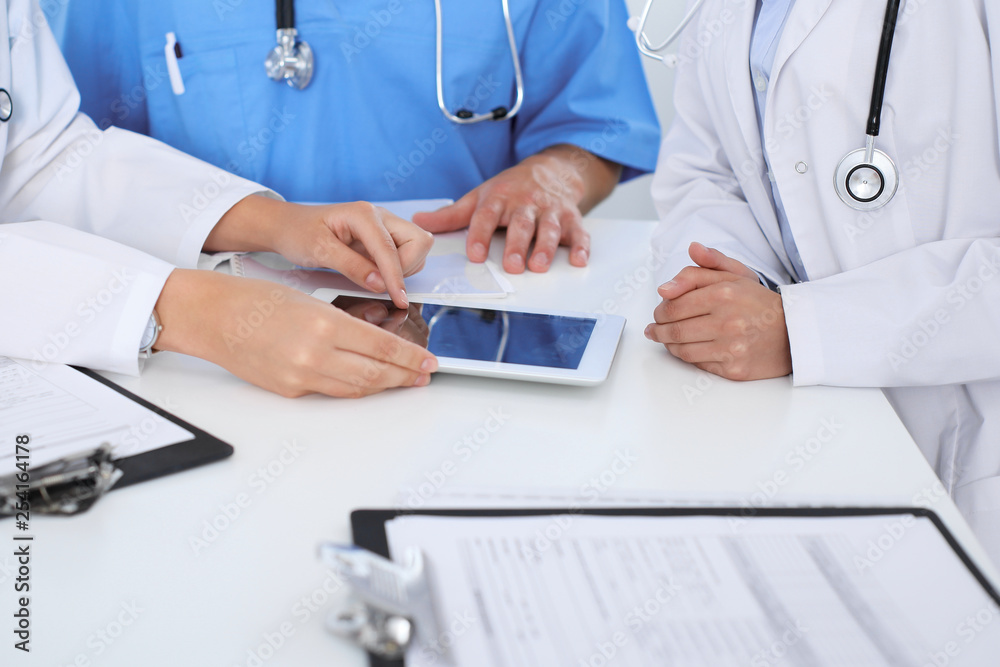 Group of doctors at medical meeting. Close up of physician using touch pad or tablet computer Group of doctors at medical meeting. Close up of physician using touch pad or tablet computer