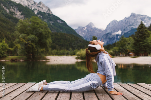 Young sports woman stretching at dock on the lake in the mountains