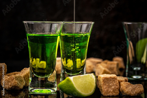 Bartender pouring absinthe in a glass, lime slices, cube brown sugar on dark background photo
