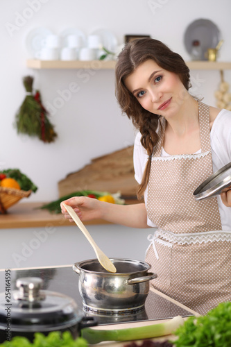 Young brunette woman cooking soup in kitchen. Housewife holding wooden spoon in her hand. Food and health concept