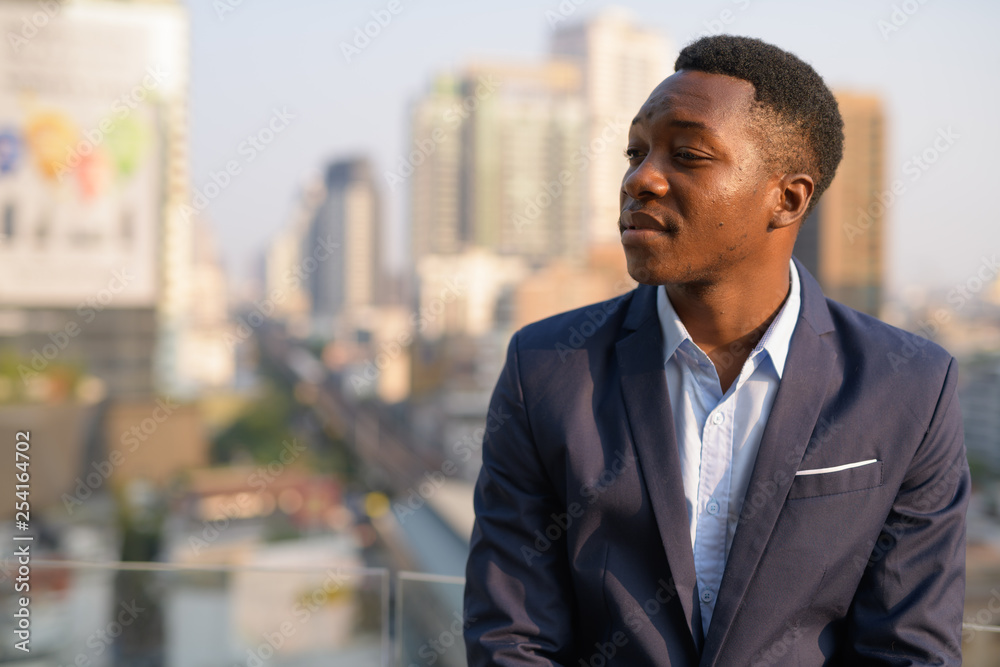 Face of young handsome African businessman thinking against view of the city