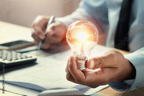 businessman hand holding lightbulb in office. concept idea saving energy