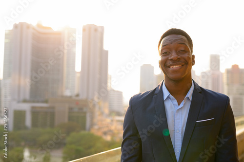 Young happy African businessman smiling against view of the city