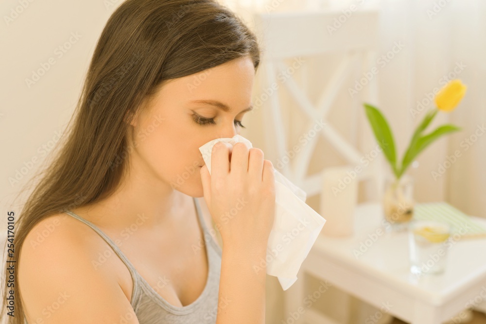 Young woman sitting in bed with handkerchief sneezing. In bedroom yellow spring flower, spring allergy on pollen. Young woman sitting in bed with handkerchief sneezing. In bedroom yellow spring flower, spring allergy on pollen.
