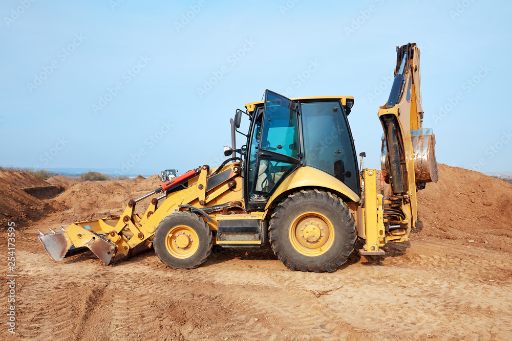 Excavator loader working at ground area on blue sky background, digging process. Yellow bucket. Outdoors, copy space. Excavator loader working at ground area on blue sky background, digging process. Yellow bucket. Outdoors, copy space.