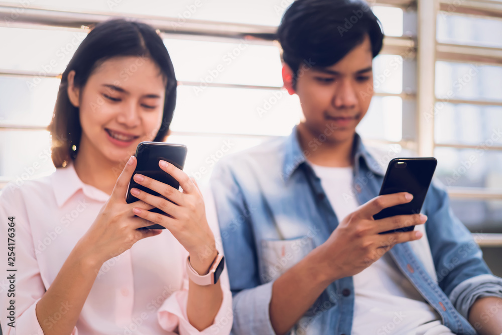 Young people are using smartphone and smiling while sitting on free time. technology concept Young people are using smartphone and smiling while sitting on free time. technology concept