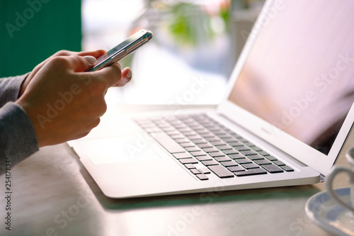 Girl works in the phone in front of a laptop