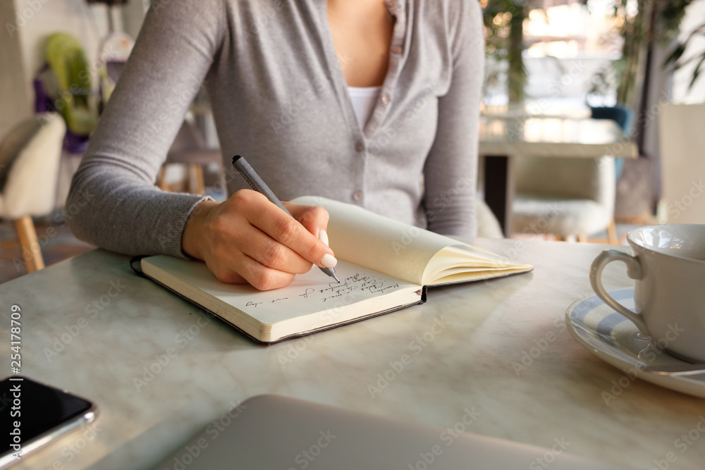 The girl takes notes in a notebook, next to a laptop and phone The girl takes notes in a notebook, next to a laptop and phone