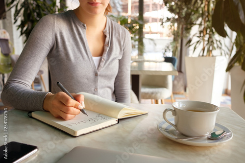 The girl takes notes in a notebook, next to a laptop and phone