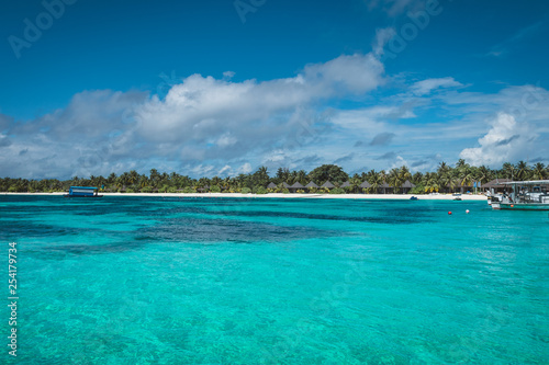 Maldives with turquoise clear water and many palm trees and clouds in the sky