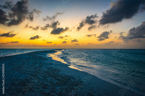 Sunset in the Maldives with reflection of the Sun in the water and blue and orange colored clouds in the sky