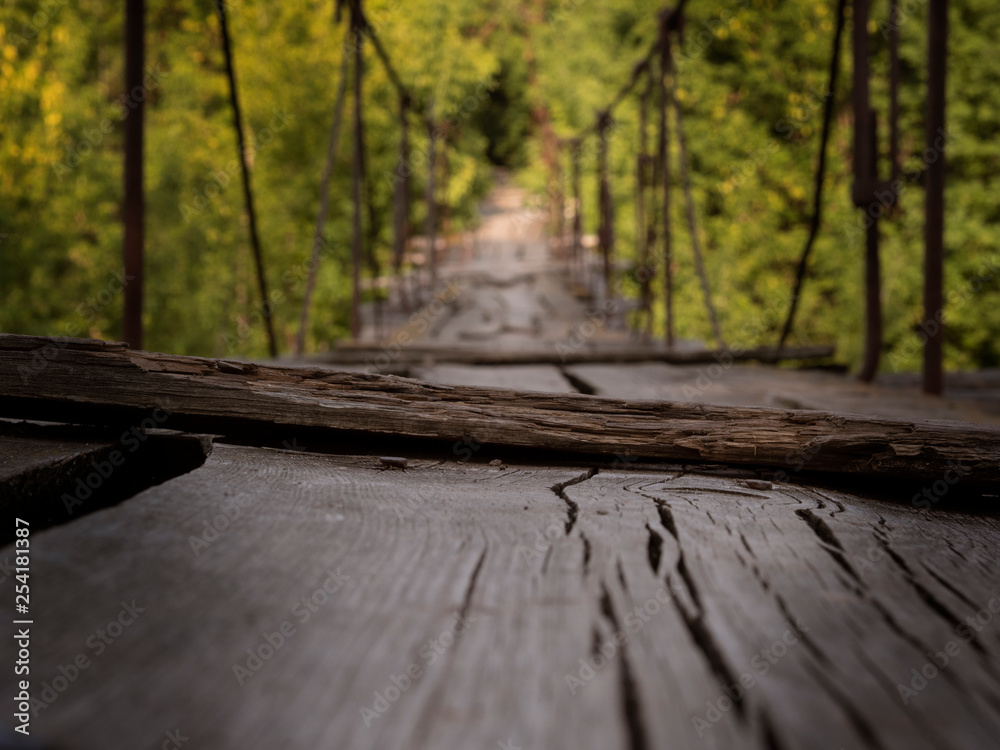 The suspension wooden bridge through the river in the forest. The long road for courageous and brave through a reservoir at the height of several meters. The suspension wooden bridge through the river in the forest. The long road for courageous and brave through a reservoir at the height of several meters.