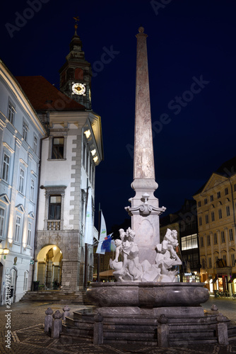 Lit Robba Fountain of the Three Rivers in the Town Square of Ljubljana capitol city of Slovenia at twilight with clock tower of the Town Hall