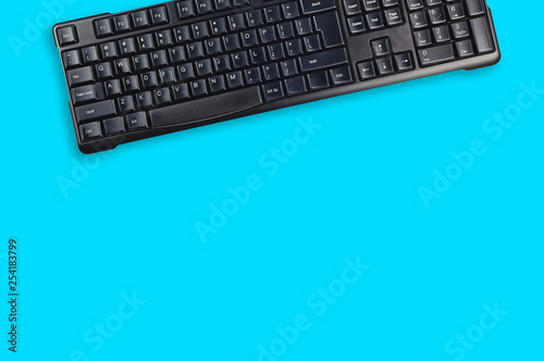 One black plastic wireless computer keyboard on blue office table. Top view. Copy space for your text. Business concept