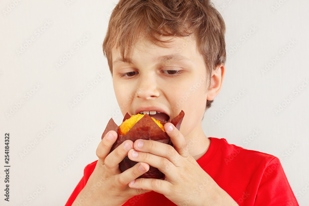 Little funny boy in a red shirt eating muffin on a white background. Little funny boy in a red shirt eating muffin on a white background.