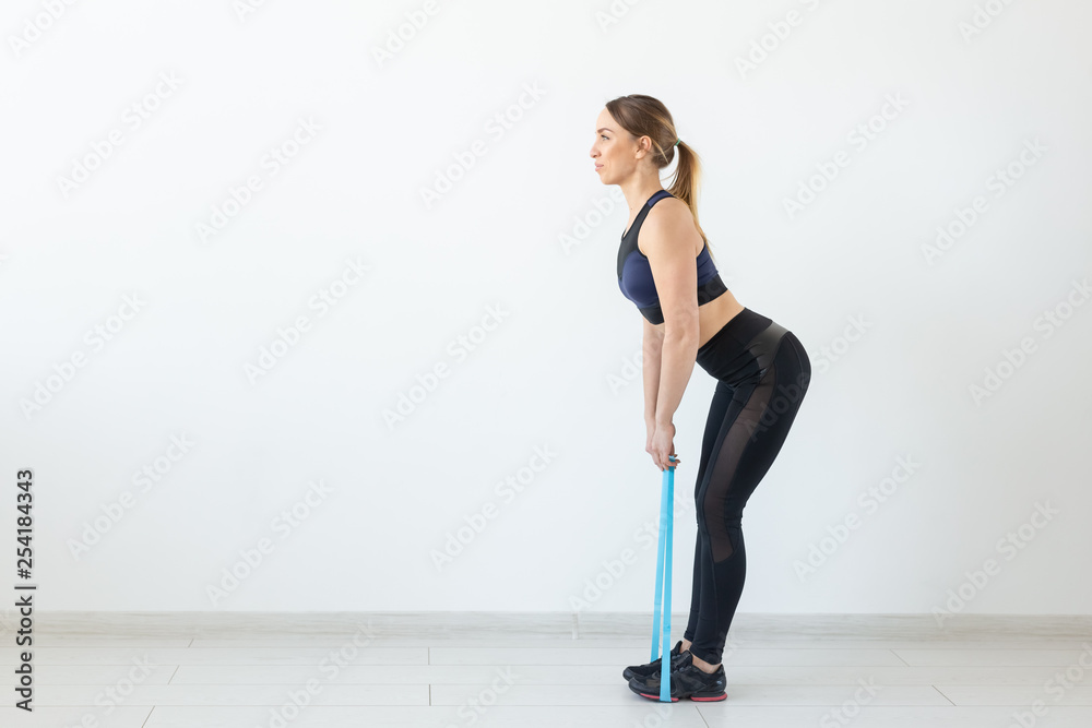 Fototapeta premium People, healthy and sport concept - Fit woman In sports clothes squatting with band