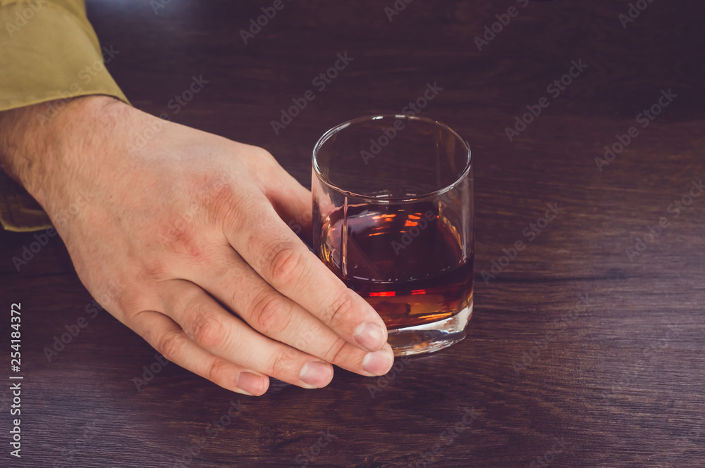 A man holding a glass of whiskey. Male hands holding a glass cup with cognac. A man holding a glass of whiskey. Male hands holding a glass cup with cognac.
