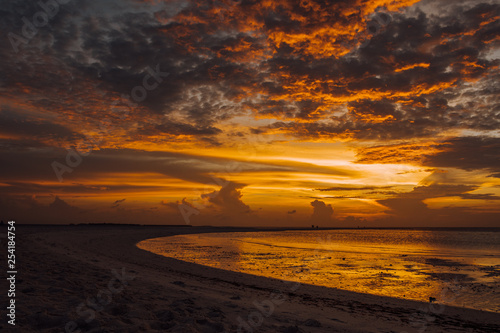 Sunset in the Maldives with reflection of the Sun in the water and blue and orange colored clouds in the sky