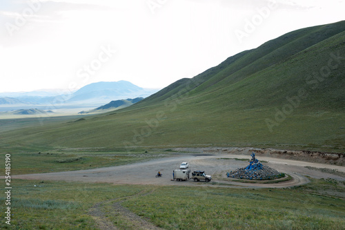 Ovoo in the mountains of Mongolia on the pass. Car with a trailer, motorcyclist and passenger car nearby