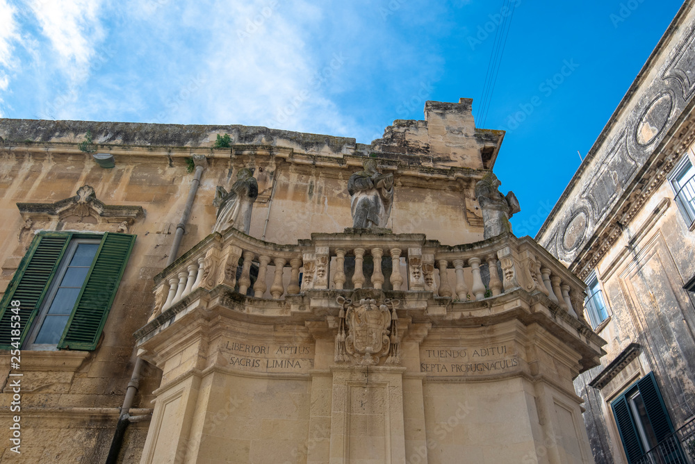 Lecce, Puglia, Italy - Medieval street and historical center in the old town. View and detail of an ancient gate or door, statues and facade of houses. A region of Apulia