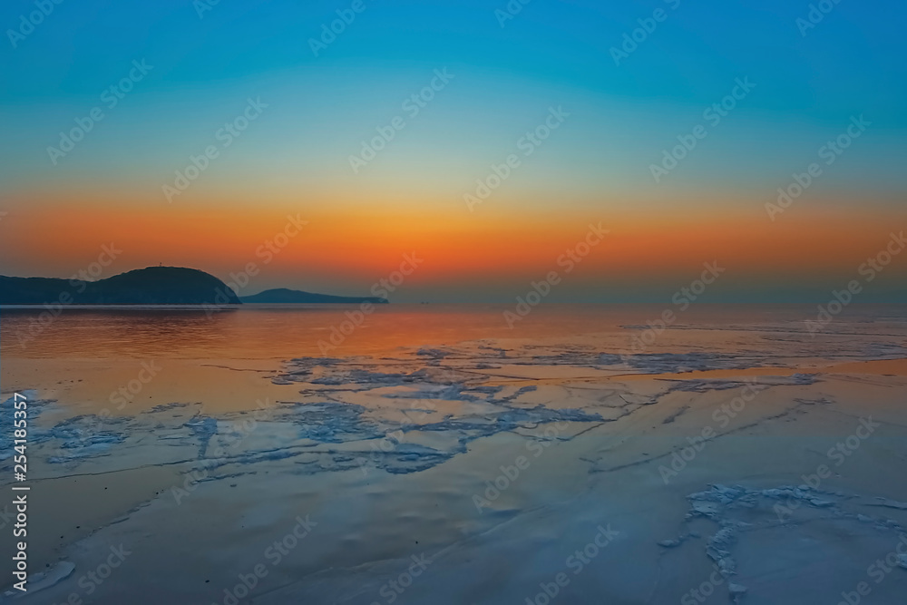 Obraz premium Seascape with bright orange sunset and ice floes at the coastline.