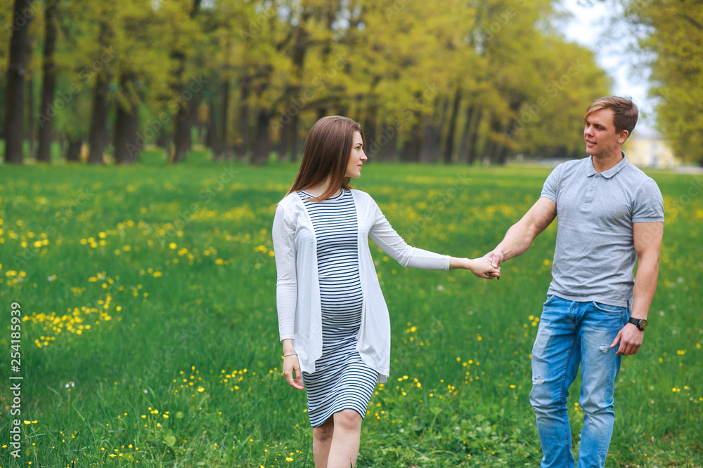 Pregnant woman with husband walking on meadow in spring day Pregnant woman with husband walking on meadow in spring day
