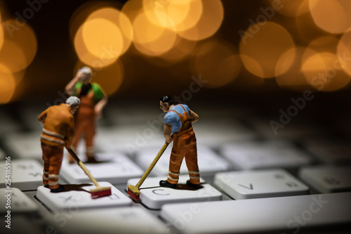 Miniature people cleaning white keyboard computer.