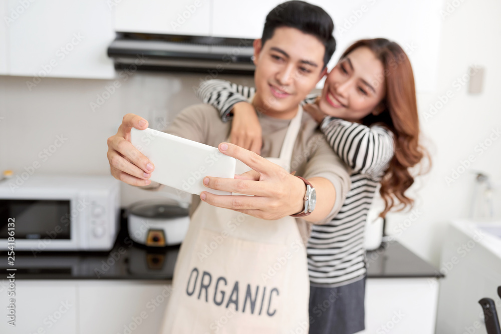 Happy couple cooking dinner and taking selfie in their loft kitchen at home. Preparing vegetable salad and photographing for social network, copy space Happy couple cooking dinner and taking selfie in their loft kitchen at home. Preparing vegetable salad and photographing for social network, copy space