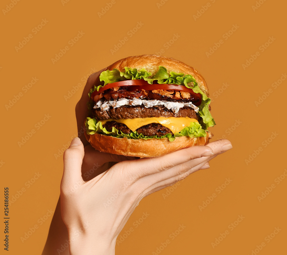 Woman hands hold big double cheeseburger burger sandwich with beef and bacon on yellow