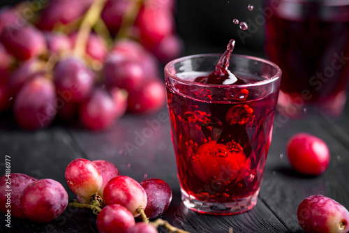 A glass of fresh grape juice, grape juice canning. Dark background, splashes and drops in a glass.